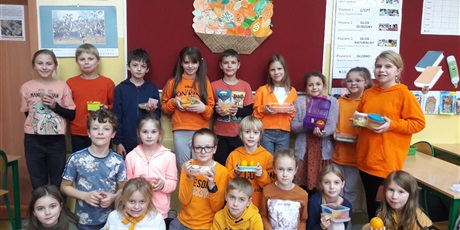 Powiększ grafikę: Wielobarwna grafika w kształcie prostokąta leżącego, przedstawiająca uczniów klasy 3d, w większości ubranych na pomarańczowo. Uczniowie trzymają w rękach pomarańczowe owoce i warzywa. W tle sala lekcyjna.
