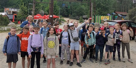 Powiększ grafikę: Barwna fotografia w kształcie prostokąta leżącego przedstawiająca kilkunastosobową grupę 9-latków z wychowawczynią na tle napisu "Adventure Park".