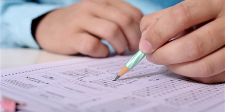 Powiększ grafikę: Barwna fotografia w kształcie prostokąta leżącego przedstawiająca dłonie ucznia, który zaznacza ołówkiem odpowiedzi w teście.