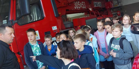 Powiększ grafikę: Na zdjęciu uczniowie klasy 5F podczas wycieczki do Straży Pożarnej. Uczniowie stoją na tle wozu strażackiego.