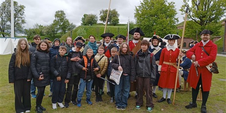Powiększ grafikę: Barwna fotografia w kształcie prostokata leżącego przedstawiająca grupę młodzieży wraz osobami w strojach historycznych.