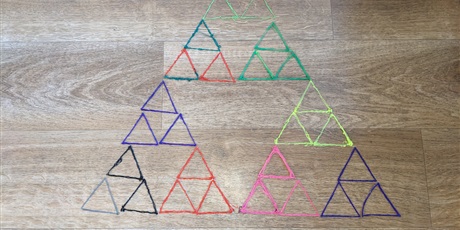 Powiększ grafikę: Kolorowy model trójkąta Sierpińskiego zbudowany z trójkątów narysowanych długopisem 3D. Fraktal leży na podłodze imitującej deski. 